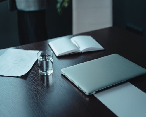A workspace with a laptop, a notebook, and a glass of water on a wooden desk